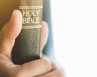 Two hands clasping a Bible with the spine showing